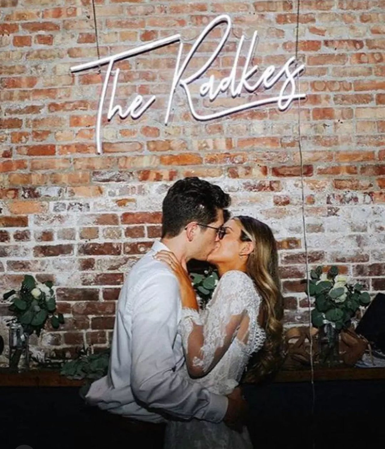 Couple kissing at their wedding under a neon sign.